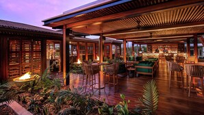 An outdoor patio area with wooden flooring, seating arrangements, and a bar area.