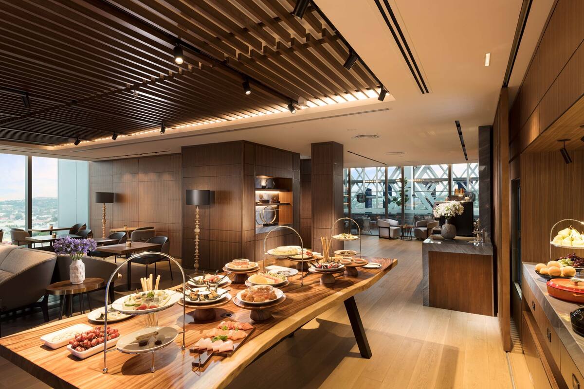 Een modern restaurantgedeelte in een hotel, met een lange buffettafel, houten plafond en grote ramen met uitzicht over de stad.