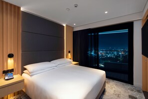 A modern hotel room with a large bed, a nightstand with a phone, and a view of the city at night. - Hilton Port Moresby Hotel & Residences (Port Moresby)