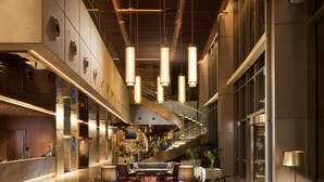 A modern hotel lobby with a central seating area, a staircase, and a reception desk.