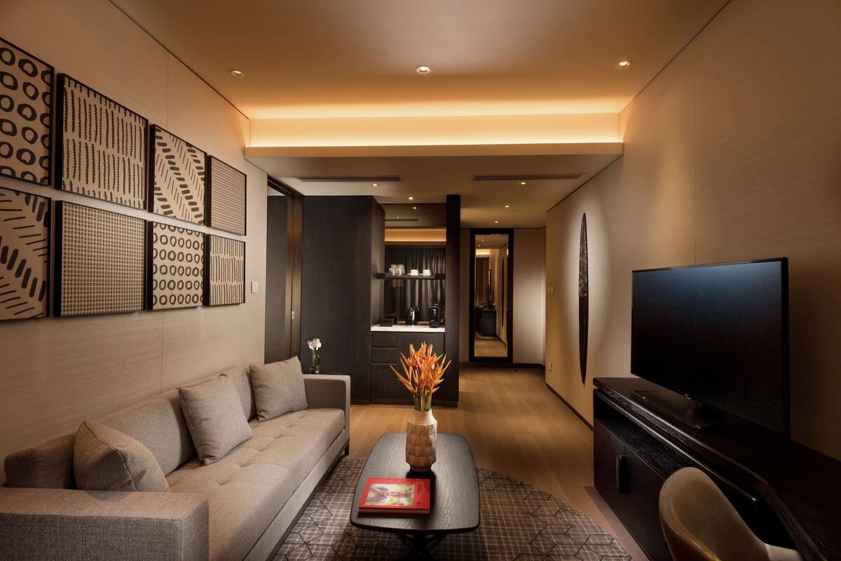 Een moderne woonkamer met een bank, een salontafel met een vaas, een flatscreen televisie en een keuken op de achtergrond.
