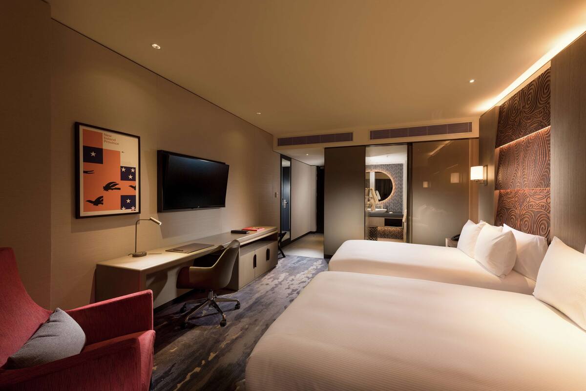 Een hotelkamer met een bed, een bureau, een stoel, een televisie en een badkamer zichtbaar door een open deur.