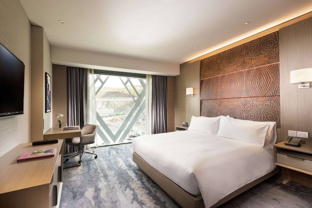 Een moderne hotelkamer met een groot bed, een bureau, een stoel, een televisie en uitzicht op de omgeving.