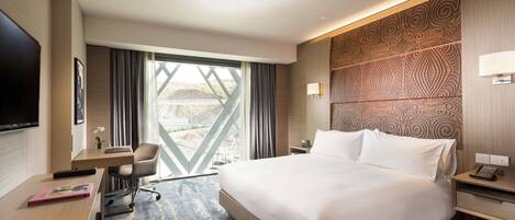Una habitación de hotel moderna con una cama grande, un escritorio, una silla, un televisor y vistas al exterior.