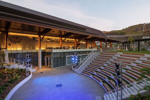 Un edificio moderno con un espacio exterior cubierto, una escalera que lleva a un nivel superior y una zona de estar con vistas al paisaje circundante.
