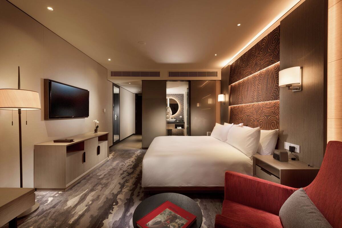 Een moderne hotelkamer met een groot bed, een televisie, een bureau en een rode fauteuil.