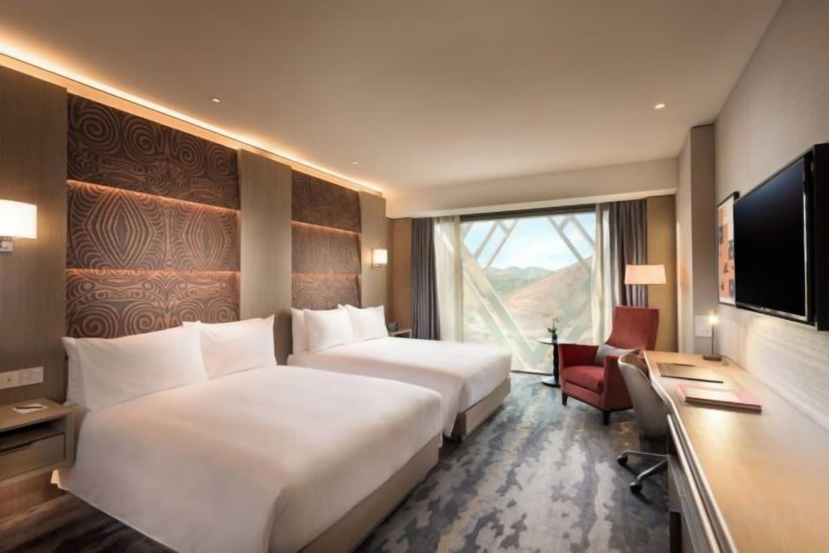 Une chambre d’hôtel avec deux lits, un bureau, une chaise, une télévision et une grande fenêtre donnant sur un beau paysage.