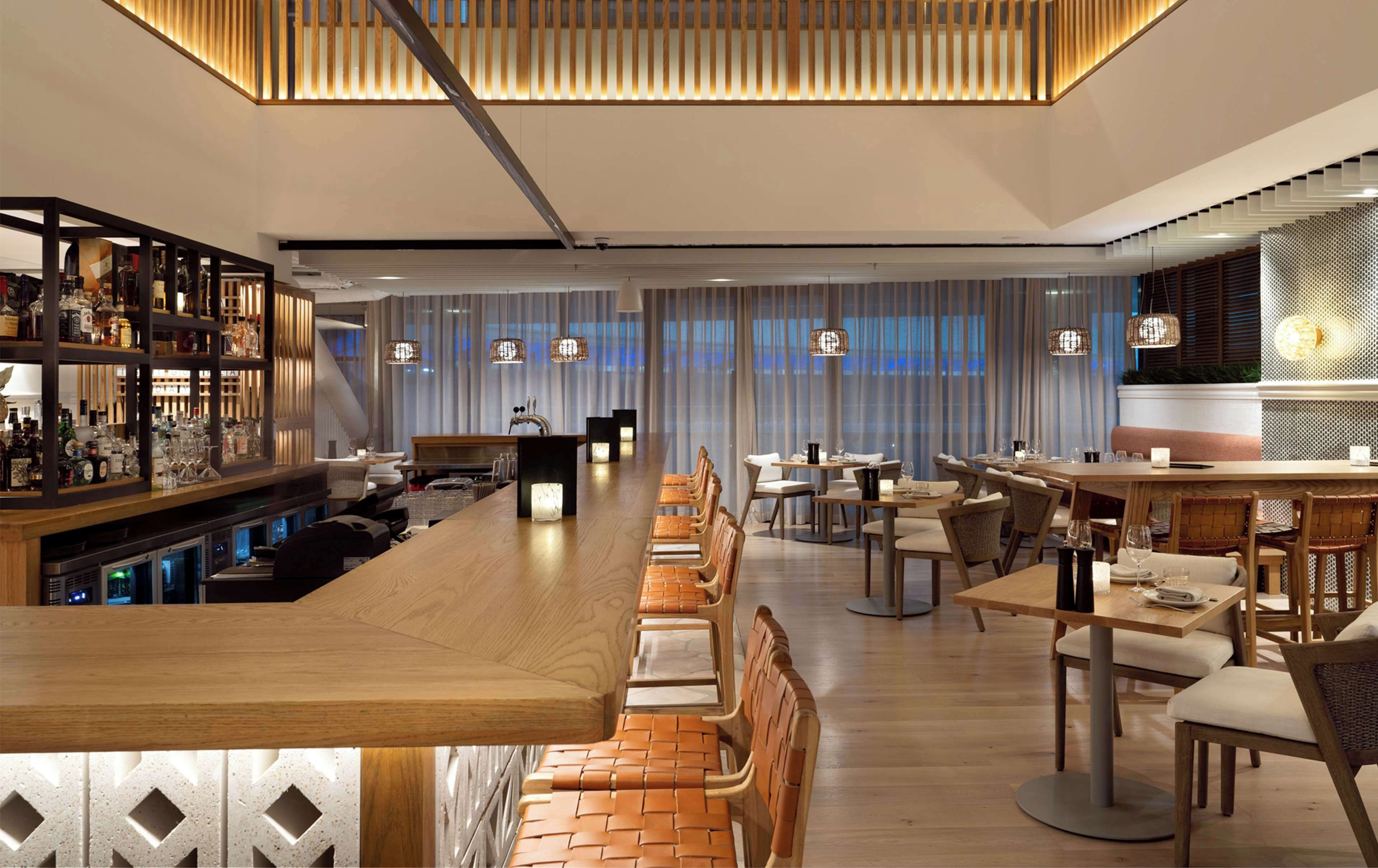 A modern bar area with a long counter, seating arrangements, and a bar stocked with various bottles.