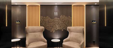 A modern lobby with two armchairs, a decorative wall with a geometric pattern, and a number '11' sign.