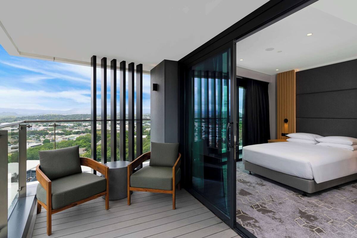 Een moderne hotelkamer met balkon, een groot bed en twee stoelen.