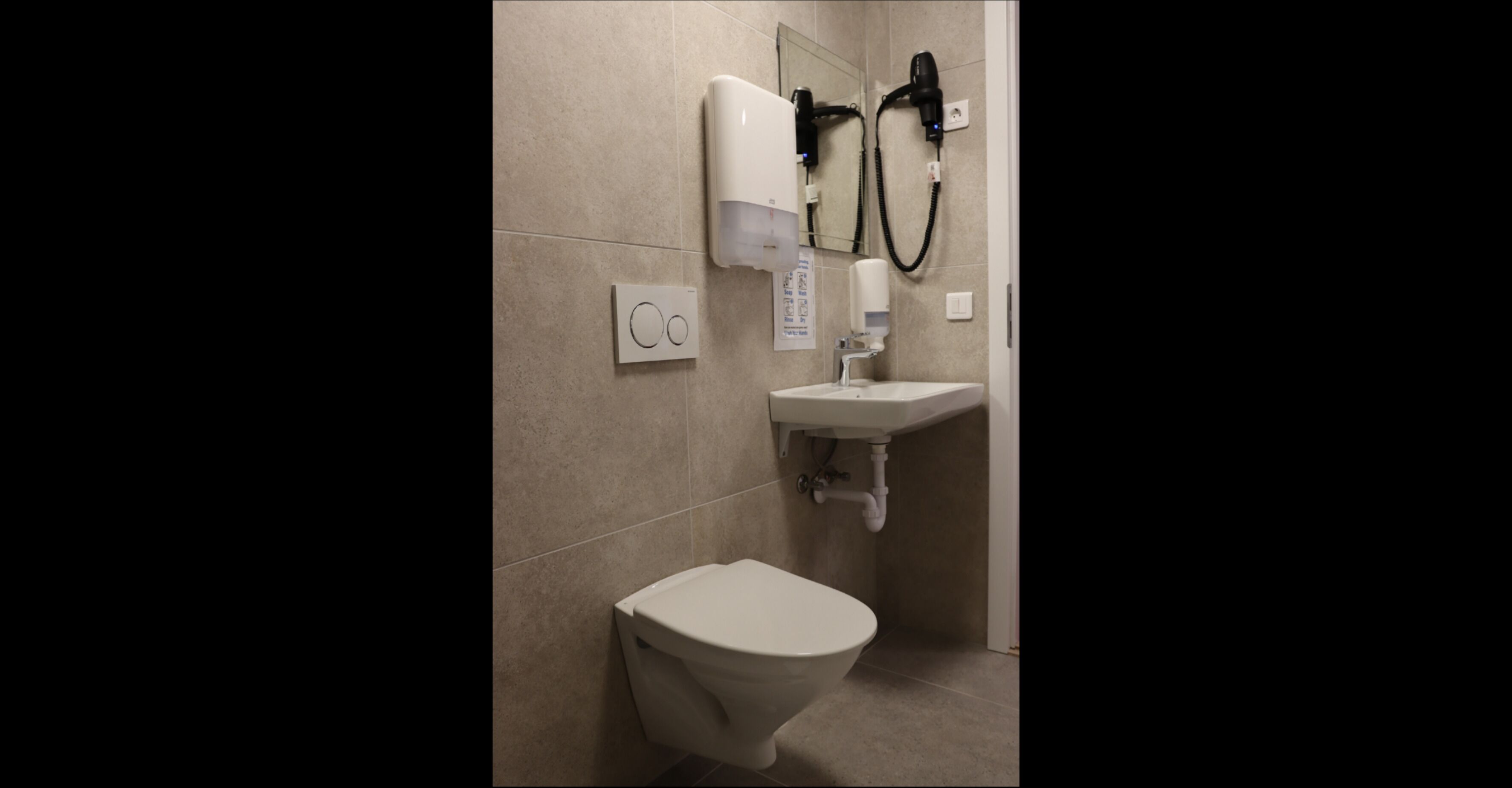 Une salle de bain équipée de toilettes, d’un lavabo et d’un sèche-cheveux fixé au mur.