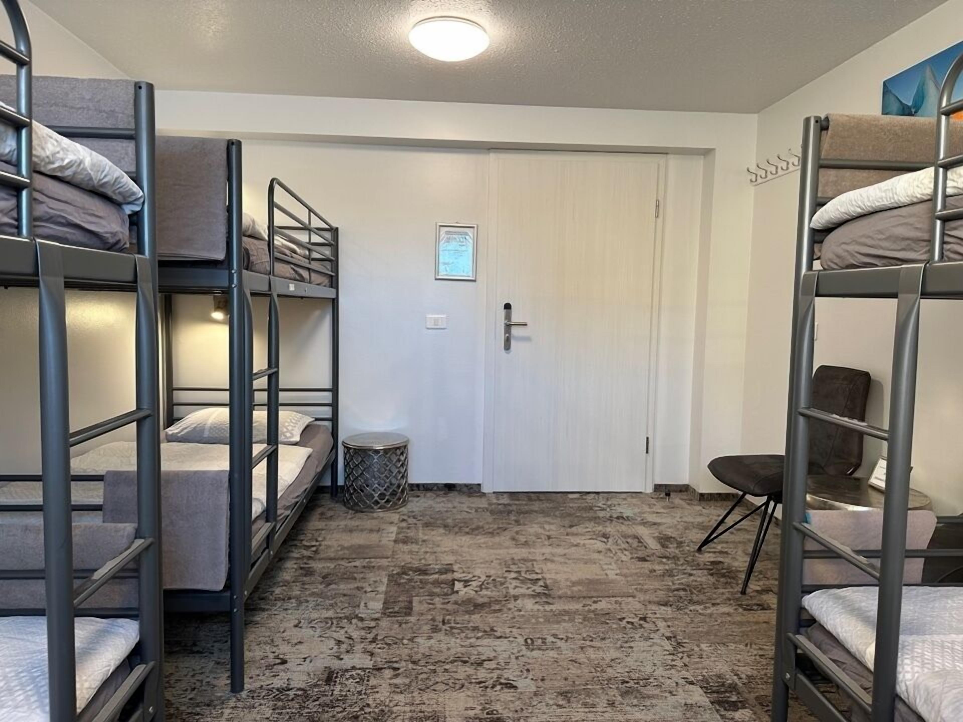 A dormitory room with bunk beds, a waste bin, a door, and a small chair.