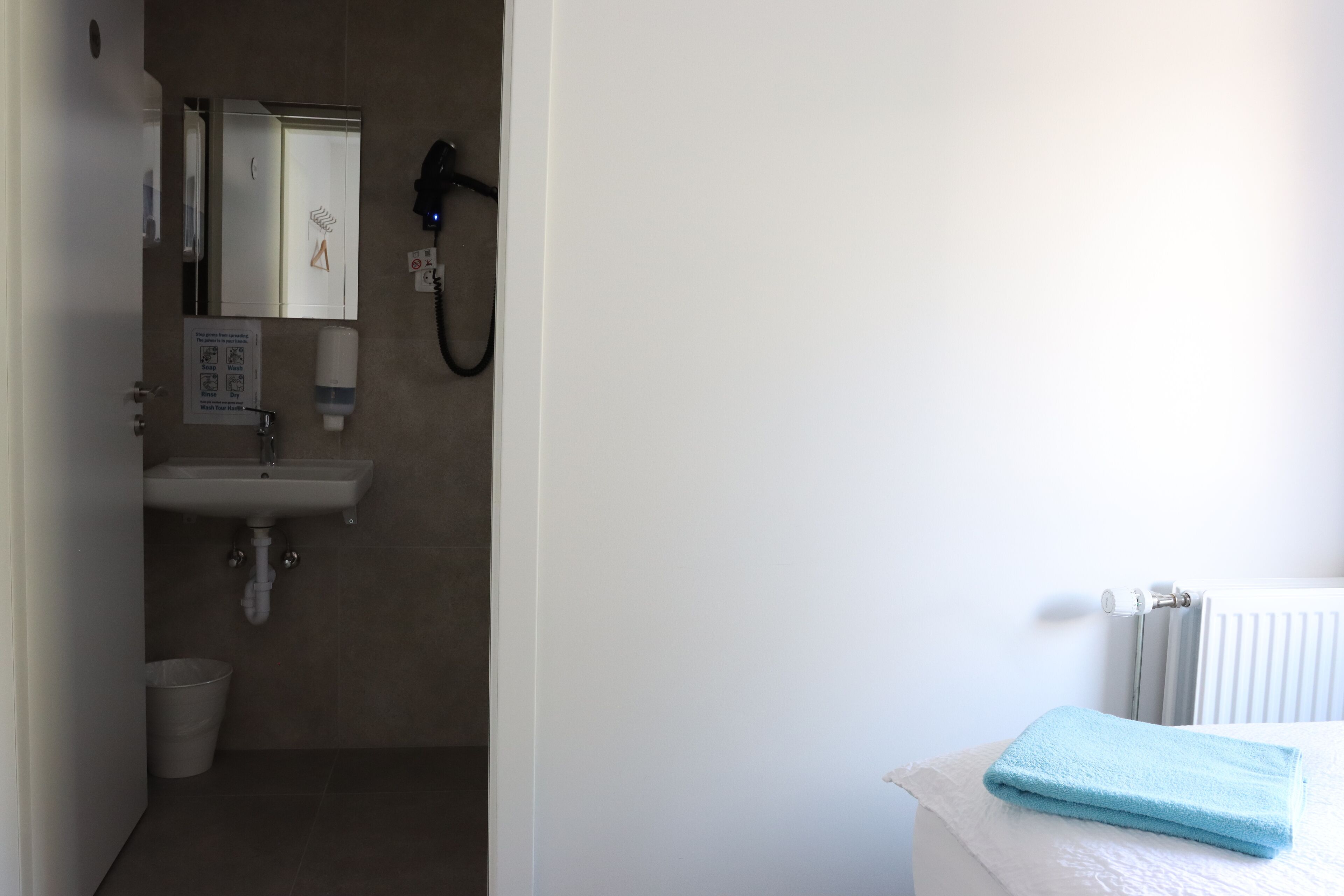A bathroom with a sink, mirror, hairdryer, and a towel on the radiator.