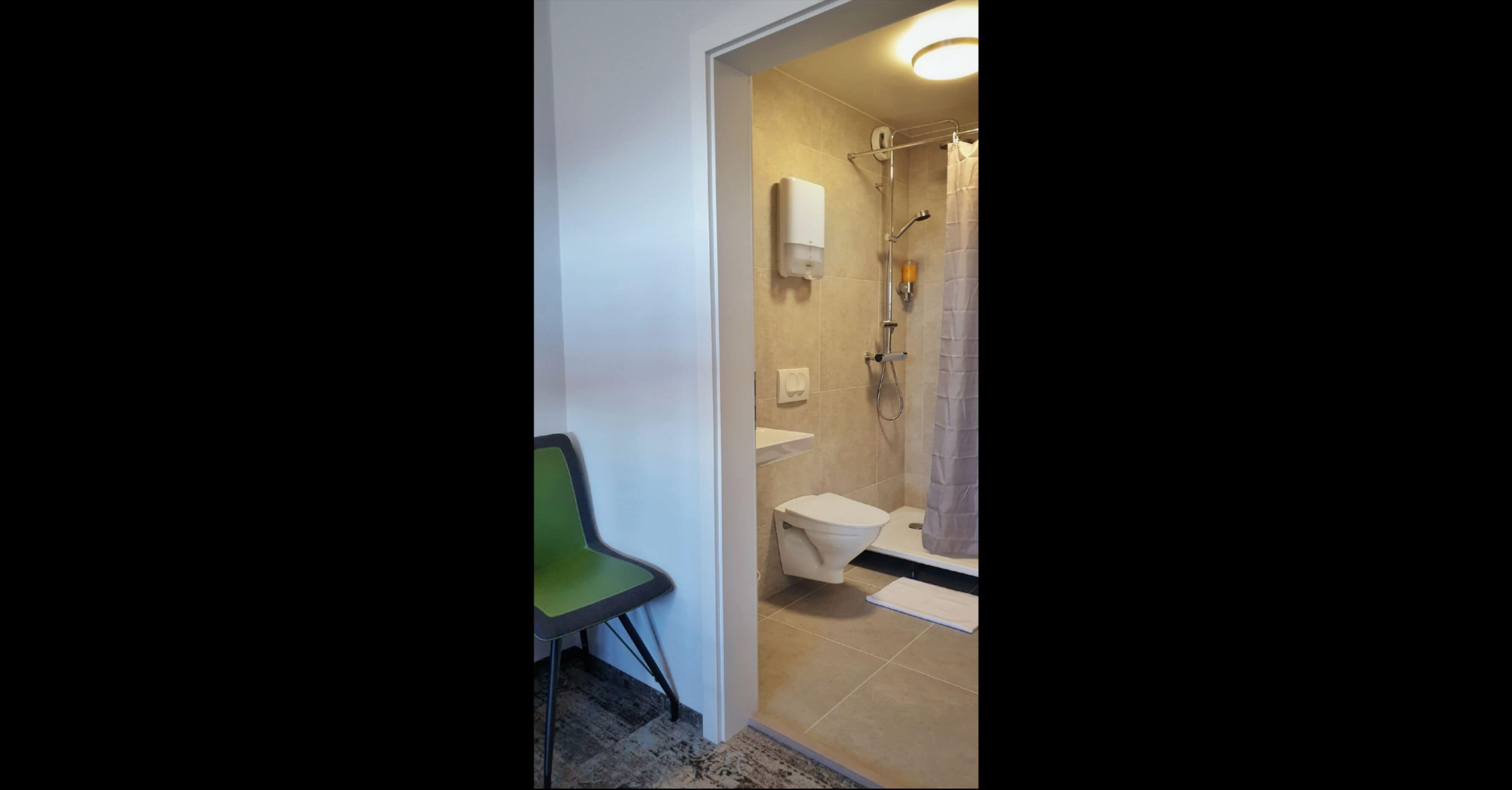 A bathroom with a toilet, shower, and a green chair.
