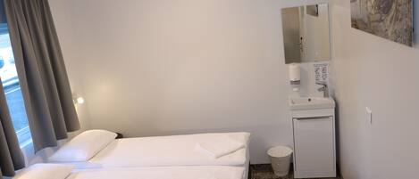 Habitación de hotel con dos camas, un lavamanos pequeño, un espejo y una ventana con cortinas.