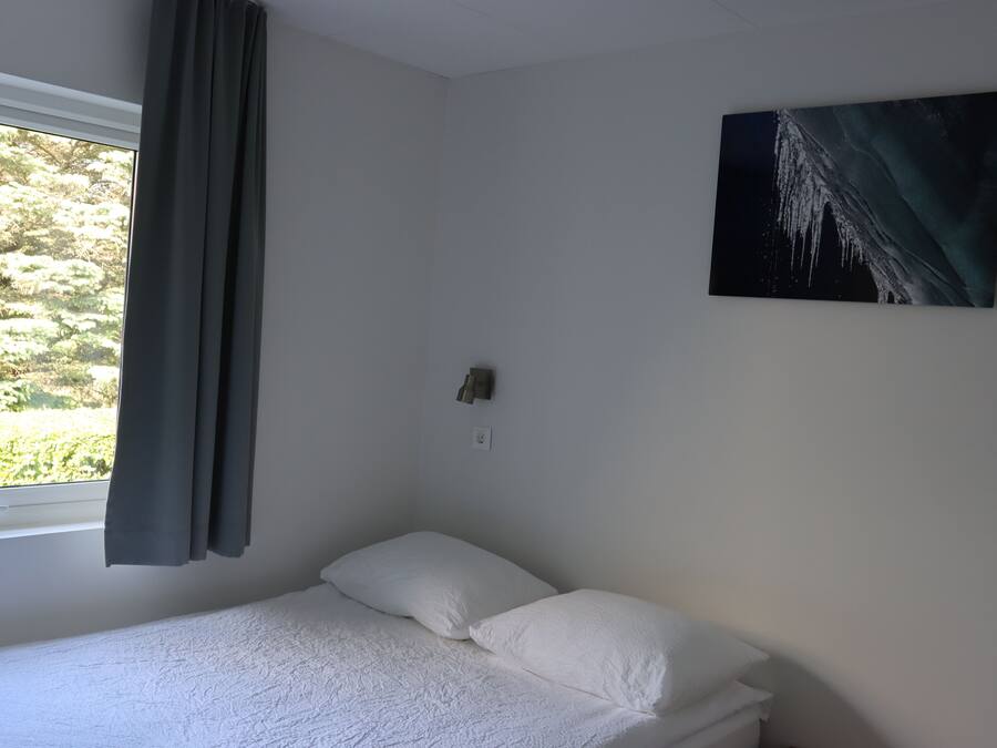 Un dormitorio con una cama individual, una ventana con cortinas y un cuadro colgado en la pared.