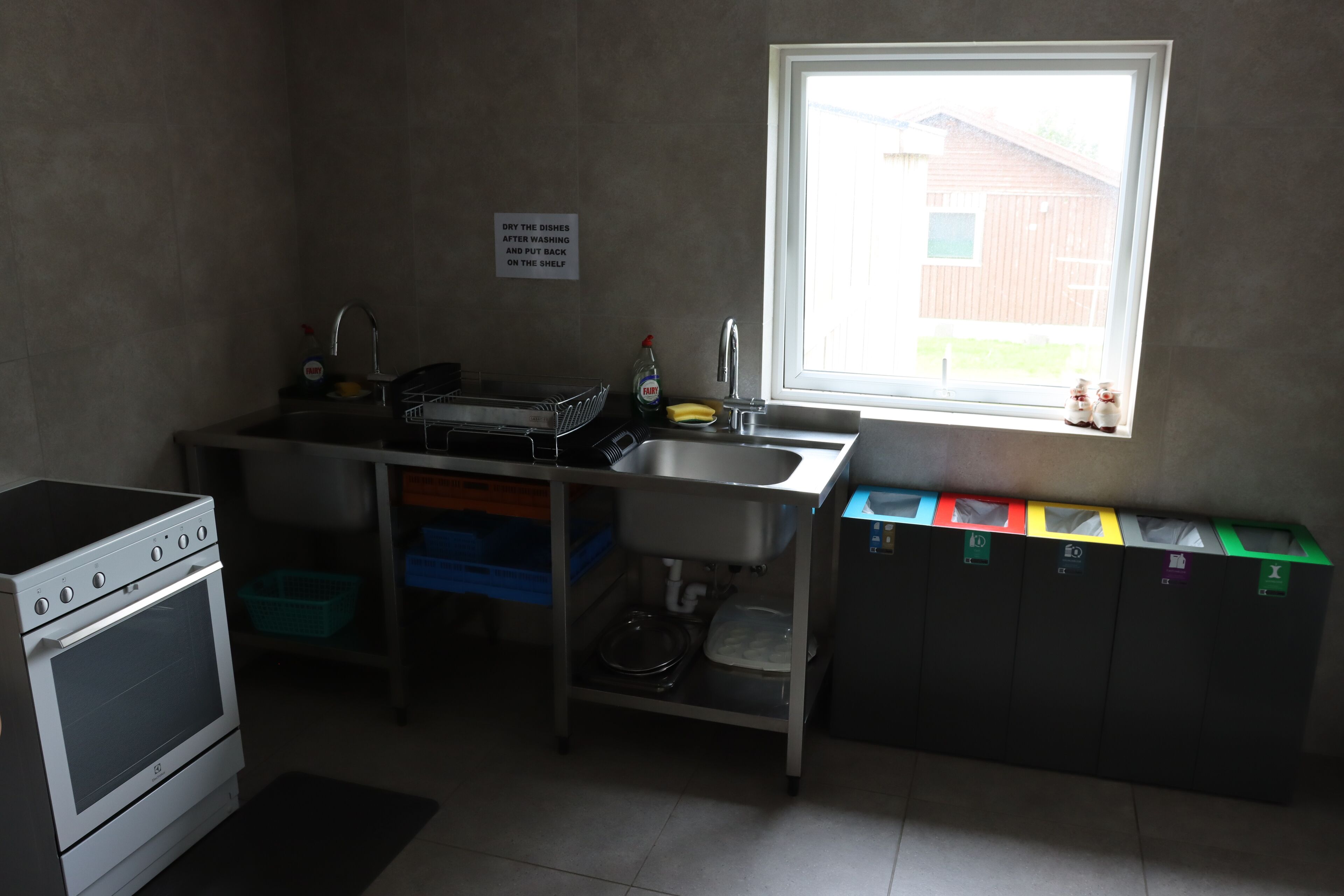 A compact kitchen with a stove, sink, and window. A sign instructs to dry dishes after washing.
