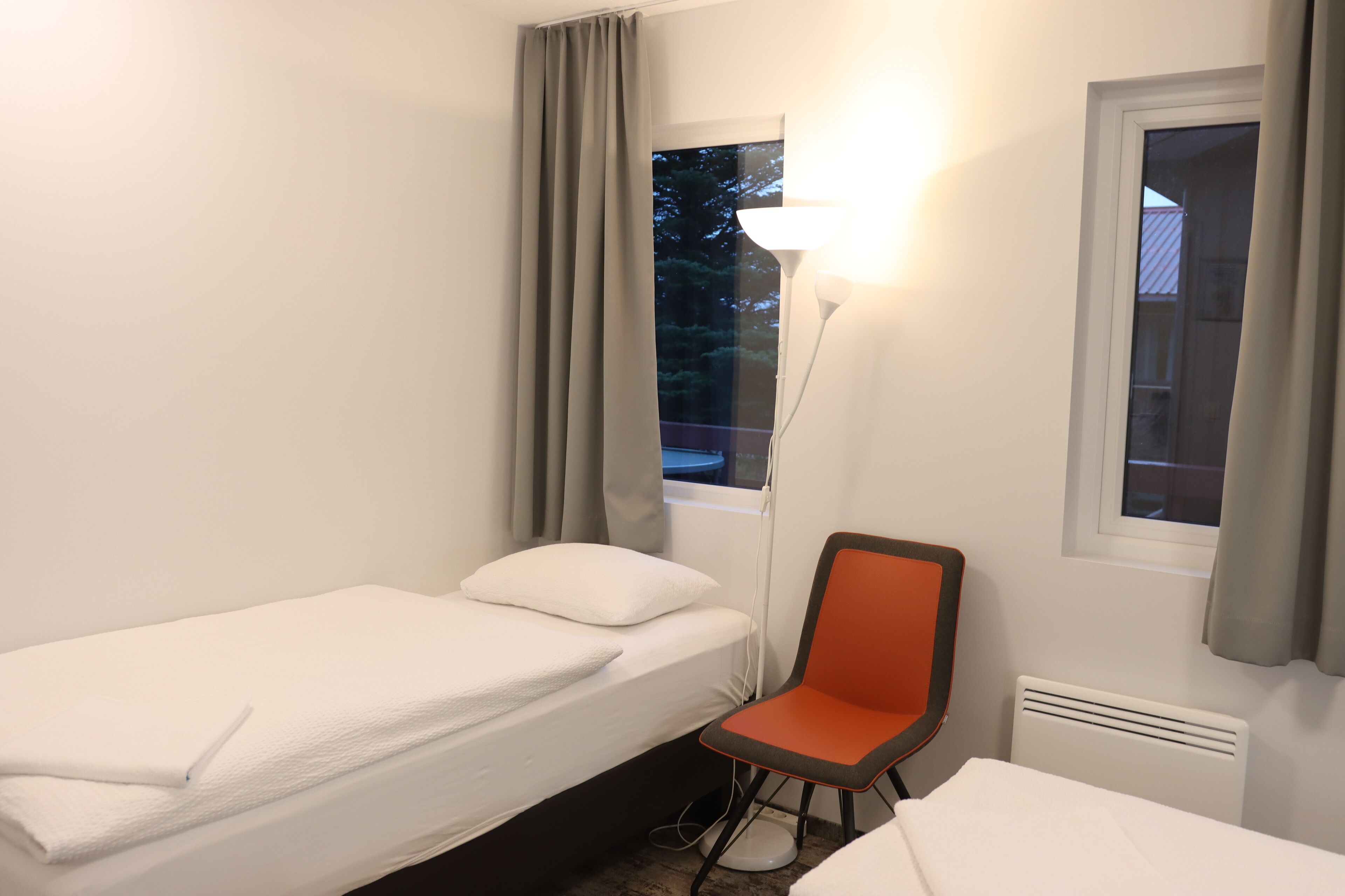 A small, clean room with a single bed, a chair, and a window with curtains.