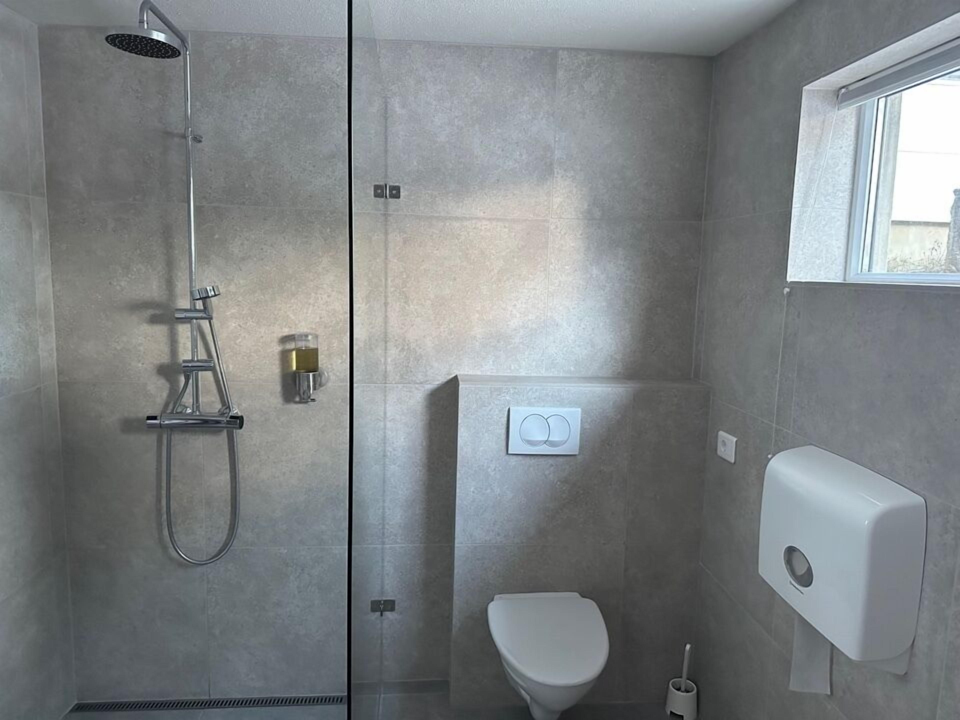 A modern bathroom with a glass-enclosed shower, a toilet, and a hand dryer.