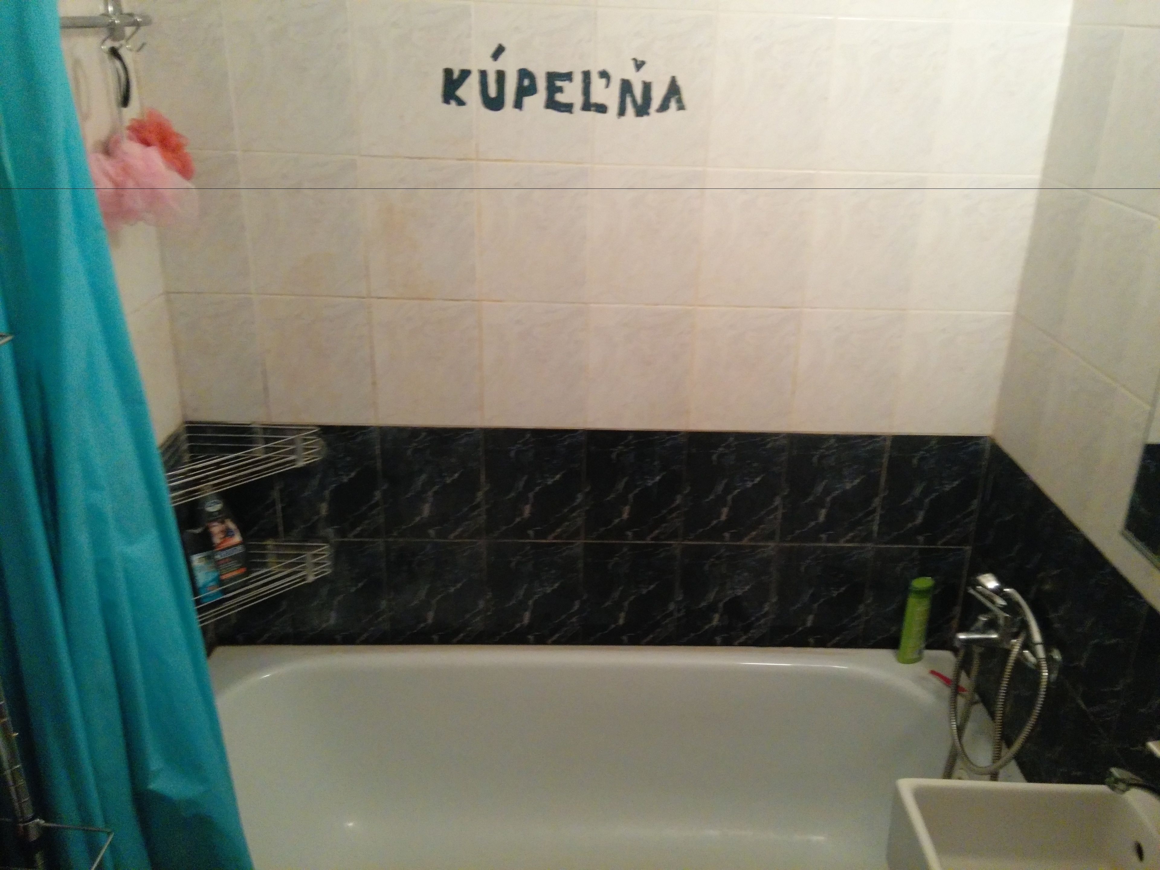 A bathroom with a bathtub, a shower, and a sink. The walls are tiled, and there is a shelf with toiletries.