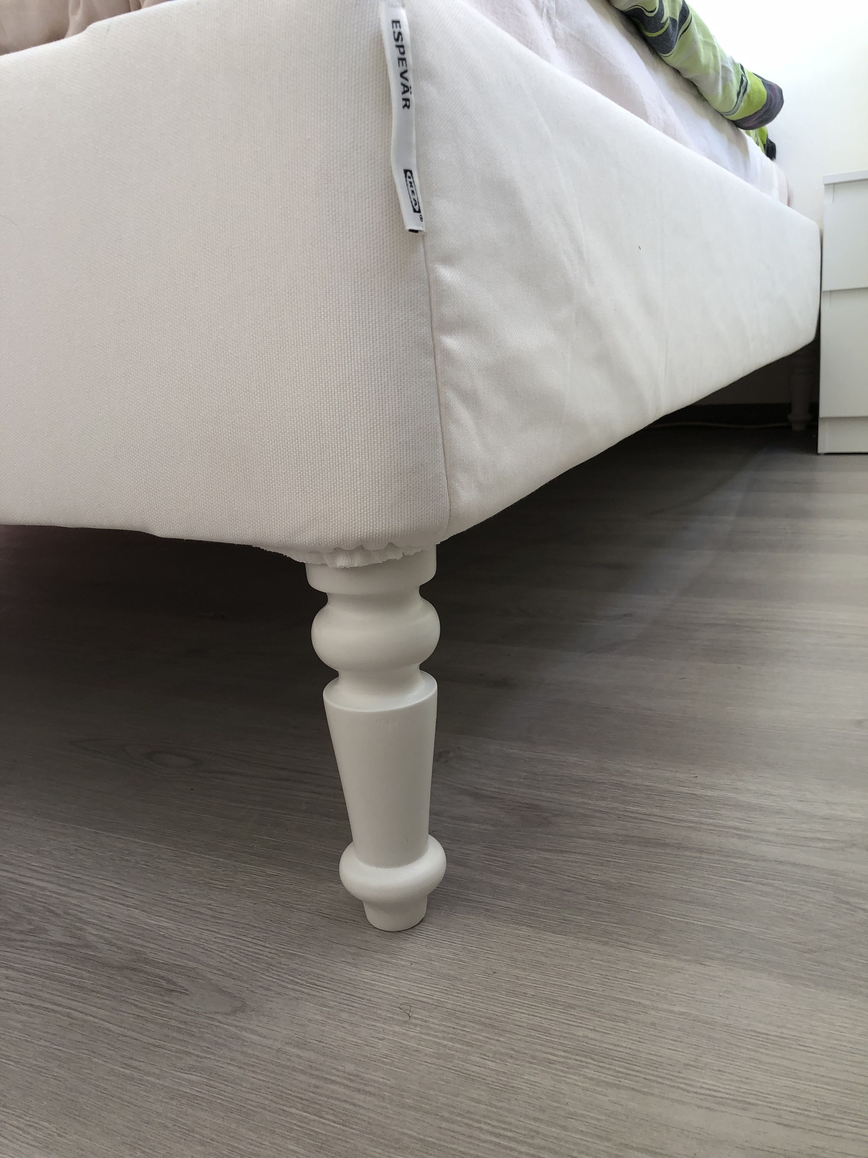 Ein weißes, gepolstertes Sofa mit Stoffetikett und Holzfuß.