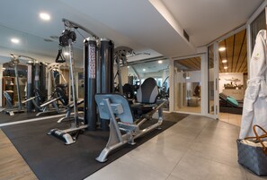 Un gimnasio moderno con diferentes máquinas de ejercicio, un muro de espejos y una puerta corredera de cristal que da a una habitación con una cama y una toalla.