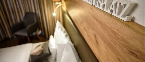 Een hotelkamer met een houten hoofdeinde, een bed met witte lakens, en een bordje aan de muur waarop 'HEINZ PLAYZ' staat.