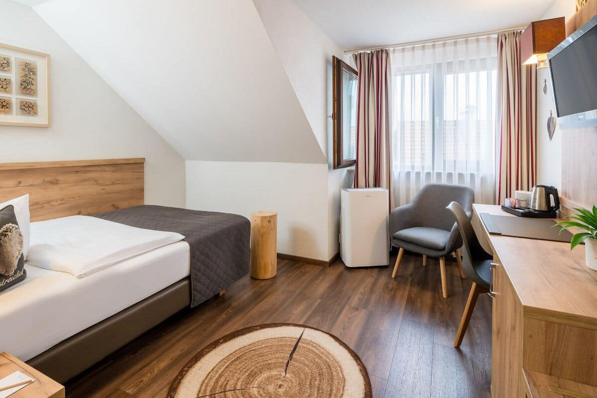Une chambre d’hôtel moderne équipée d’un lit, d’un bureau, d’une chaise et d’une grande fenêtre avec des rideaux.