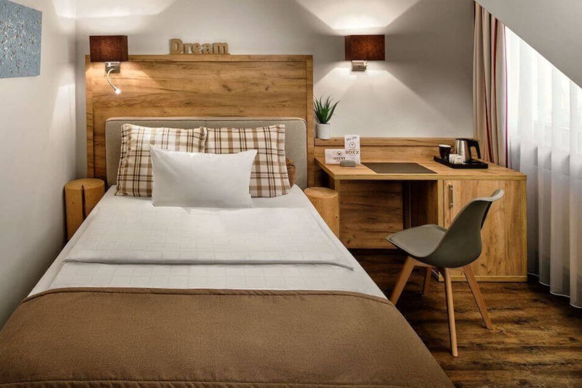 Une chambre d’hôtel équipée d’un lit, d’un bureau, d’une chaise, d’une table de chevet et d’une lampe fixée au mur.