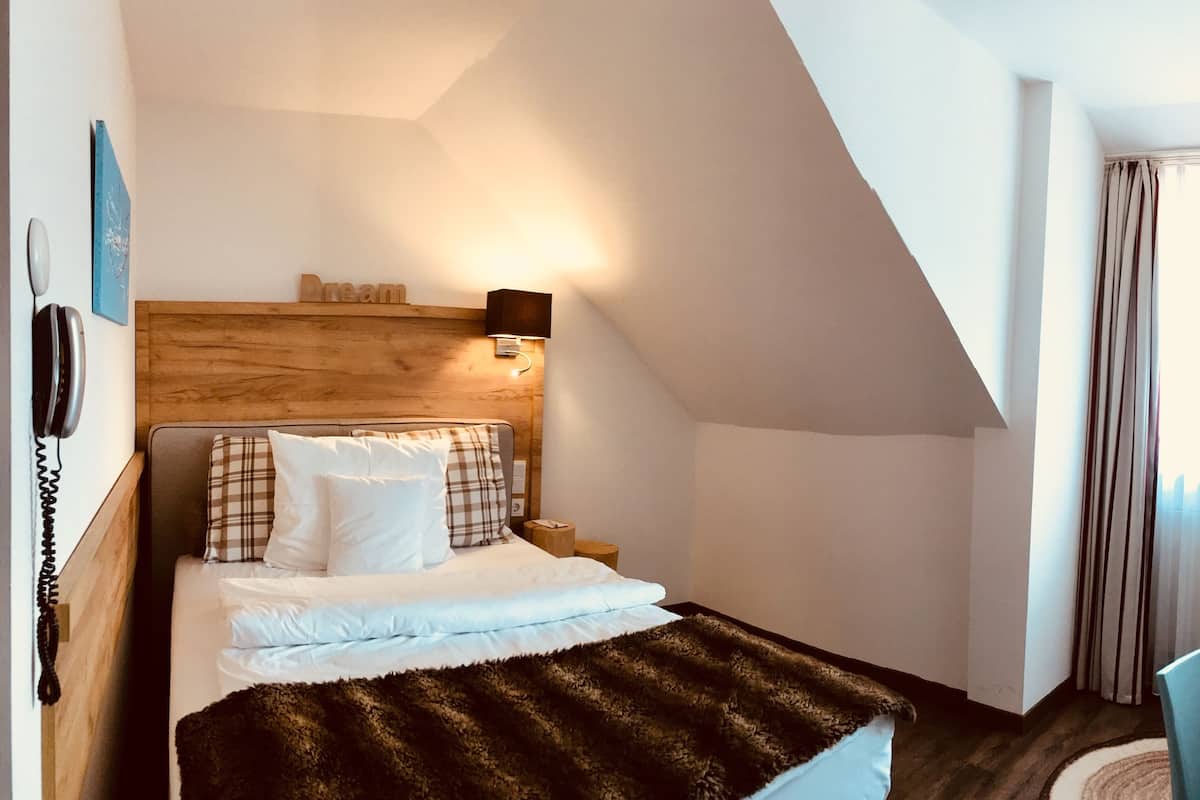Une chambre d’hôtel comprenant un lit, une table de chevet, une chaise, une télévision et une fenêtre avec des rideaux.