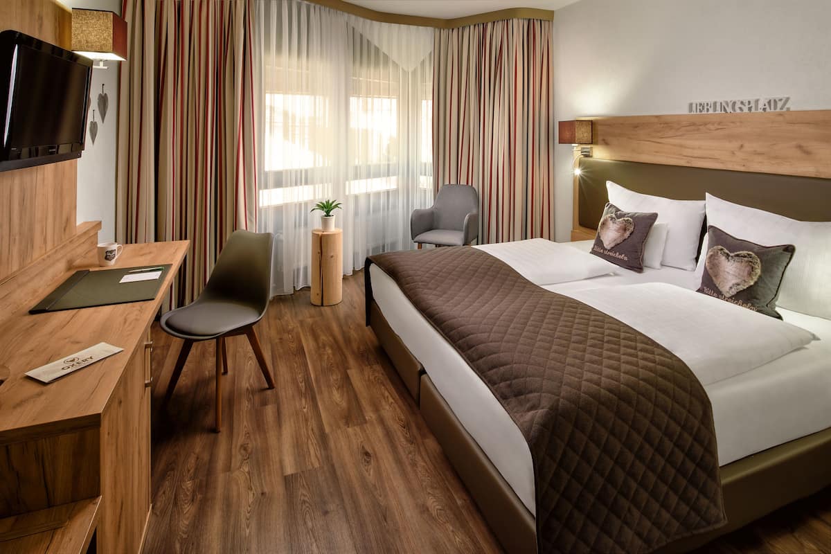 Une chambre d’hôtel avec un lit, un bureau, une chaise, une télévision et des rideaux.