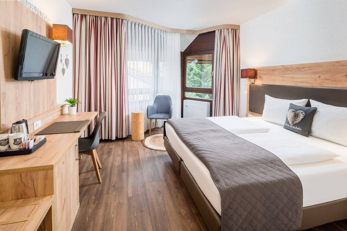 Une chambre d’hôtel avec un lit, un bureau, une chaise, une télévision et une fenêtre avec des rideaux.