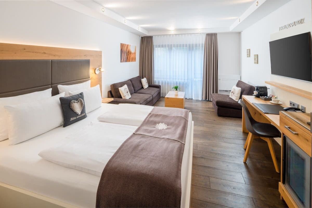 Une chambre d’hôtel avec deux lits, un bureau, une télévision et une grande fenêtre avec des rideaux.