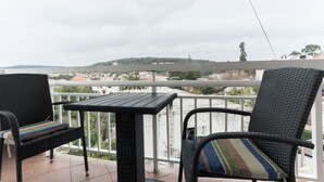 En balkon med fletningsmøbler og et bord, med udsigt over et boligområde med huse og grønt.