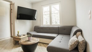 En moderne stue med en grå hjørnesofa, et rundt sofabord og et fladskærms-tv monteret på væggen.