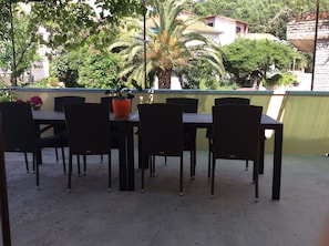 An outdoor patio with a table and chairs, surrounded by greenery and buildings in the background. - Apartmani Goic (Jelsa)