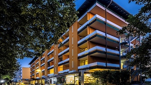 A multi-story hotel with a modern design, featuring balconies on each floor and a ground-level commercial area with shops. - Kurhotel Panland (Bad Fuessing)