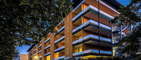 A multi-story hotel with a modern design, featuring balconies on each floor and a ground-level commercial area with shops.