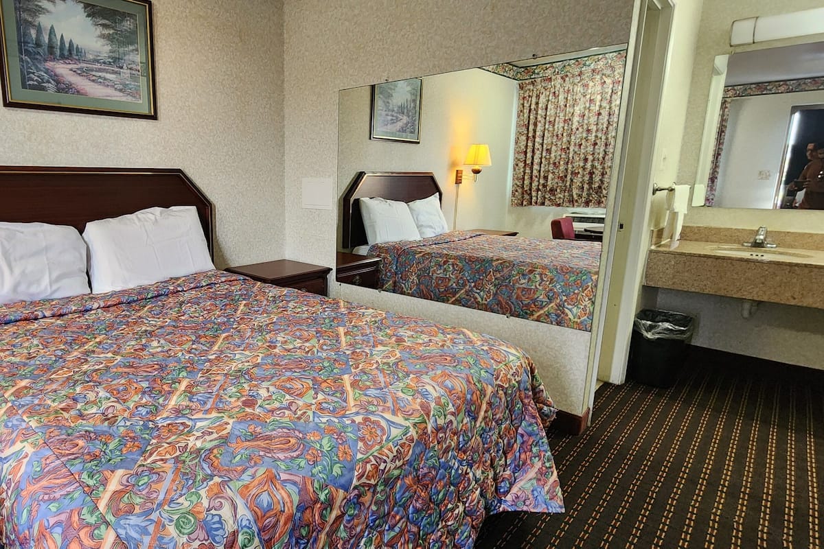 Une chambre d’hôtel avec un grand lit, une table de chevet, une lampe, un miroir et une salle de bain équipée d’un lavabo et de toilettes.