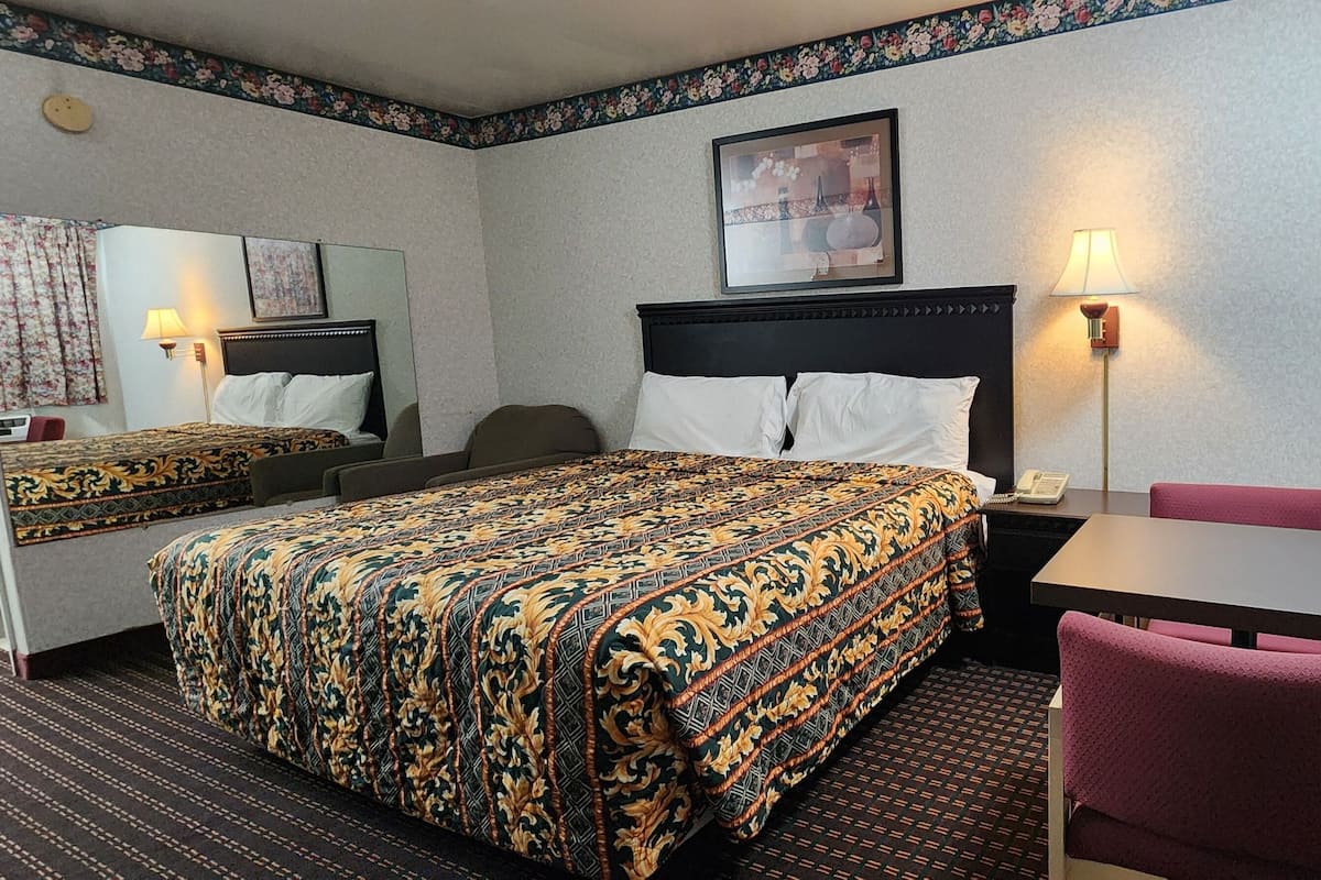 Une chambre d’hôtel avec un grand lit, un bureau, une chaise, une lampe et un appareil de climatisation.
