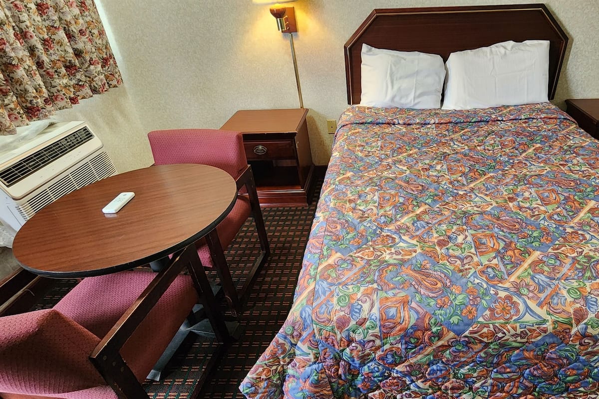 Une chambre d’hôtel comprenant un lit, un petit bureau, une chaise, une table et un climatiseur fixé au mur.