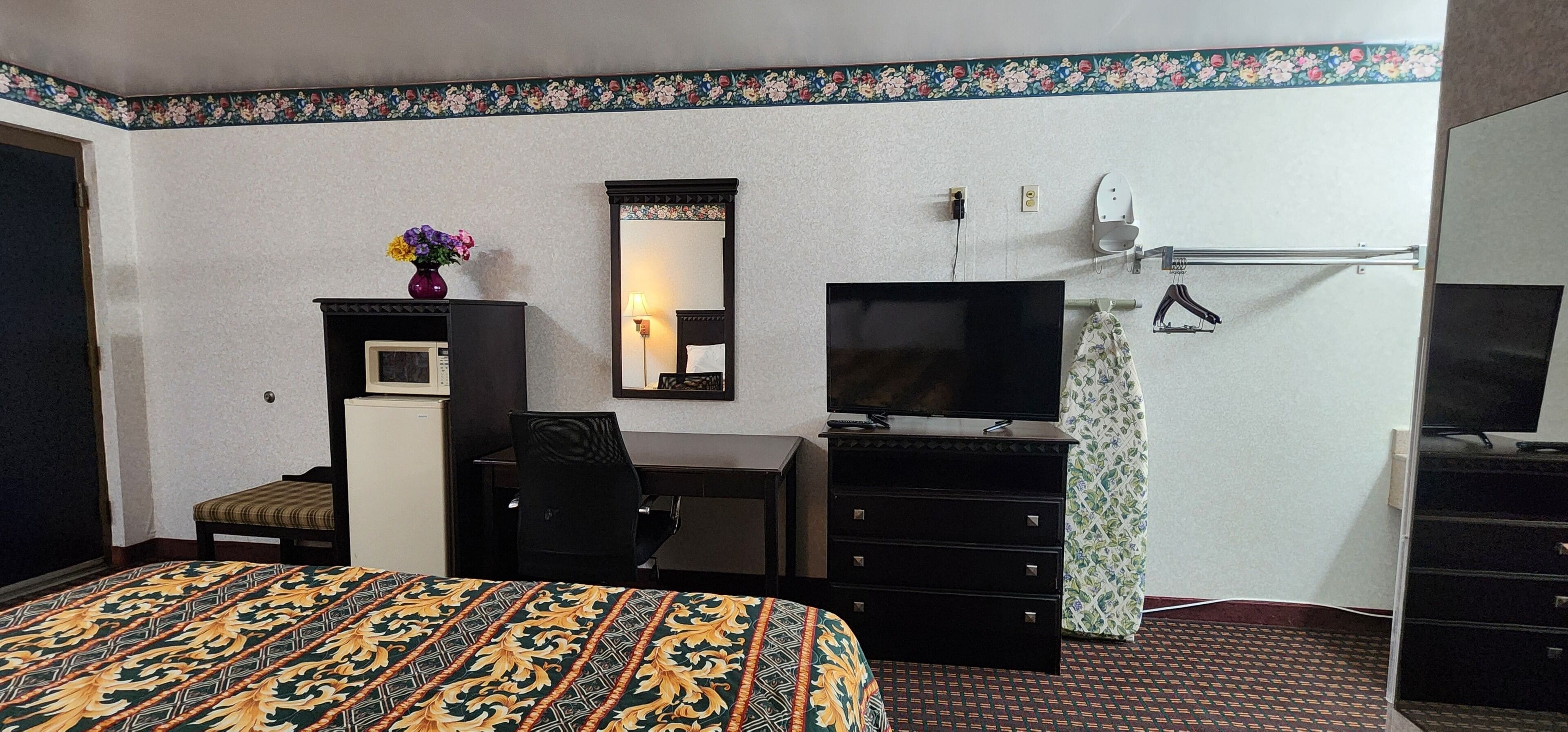 Ein Hotelzimmer mit Bett, Schreibtisch, Fernseher, Kommode und Spiegel.