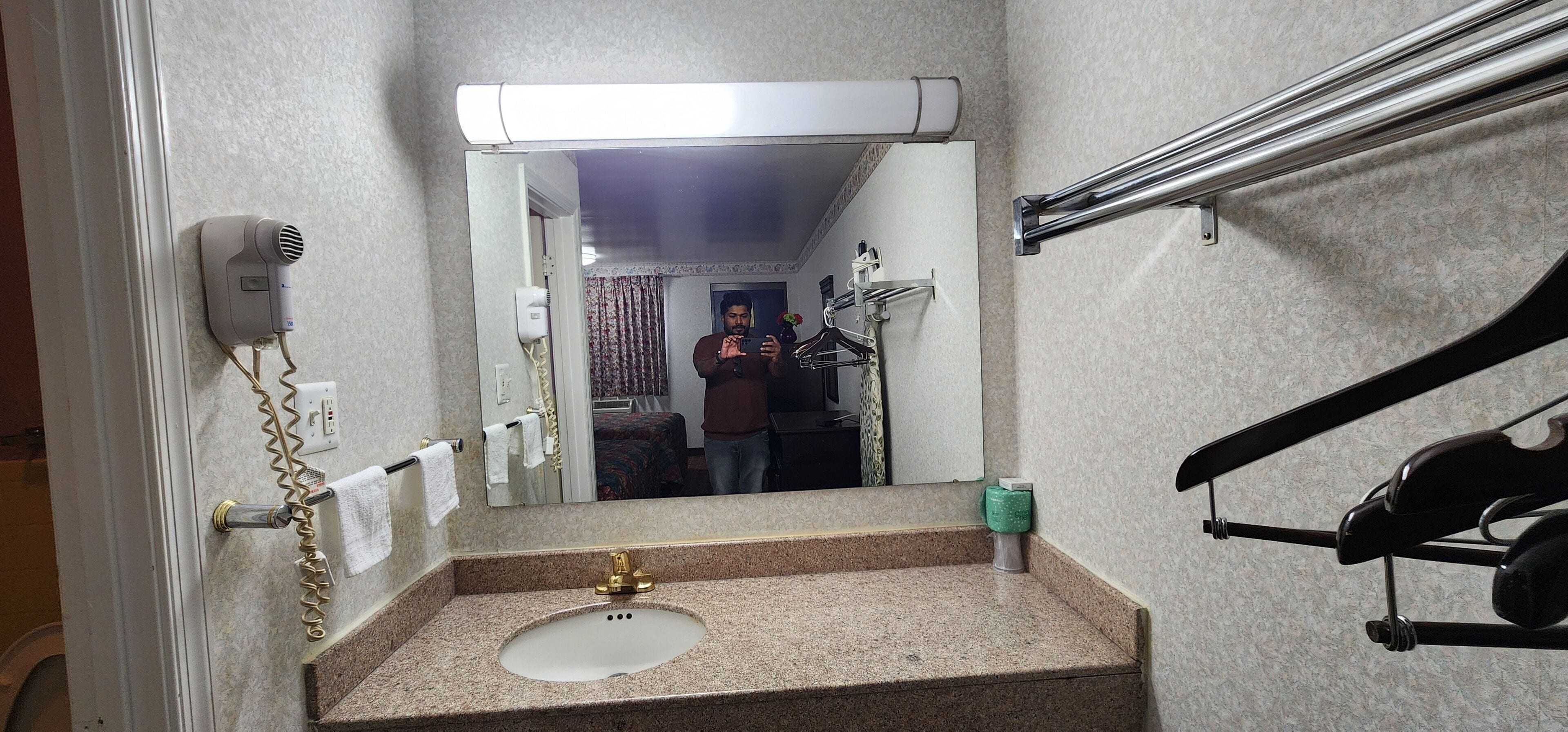 A bathroom with a sink, mirror, towel rack, and a hairdryer on the wall.