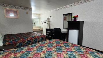 A hotel room with two beds, a desk, a mirror, a dresser, and a refrigerator.