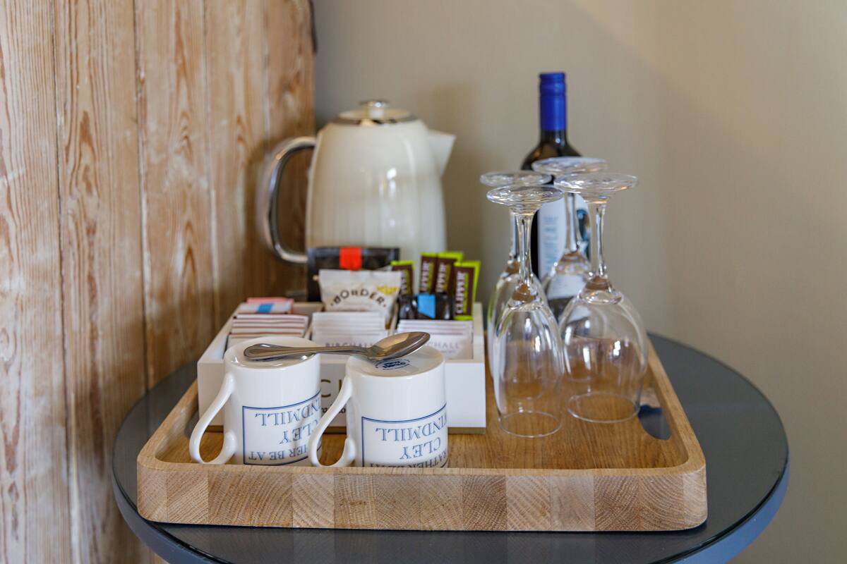 A tray with two coffee mugs, a teapot, a bottle, and a glass carafe on a glass table.