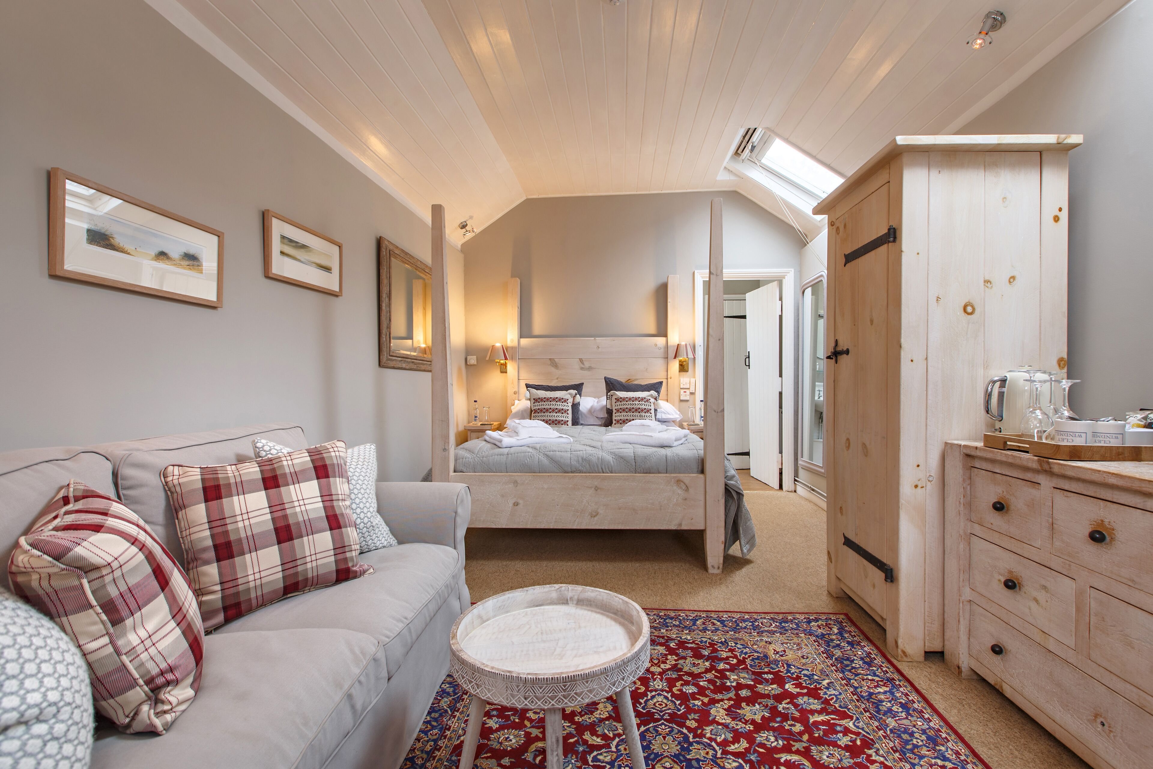 A bedroom with a bed, a sofa, a small round table, a dresser, and a red patterned rug.