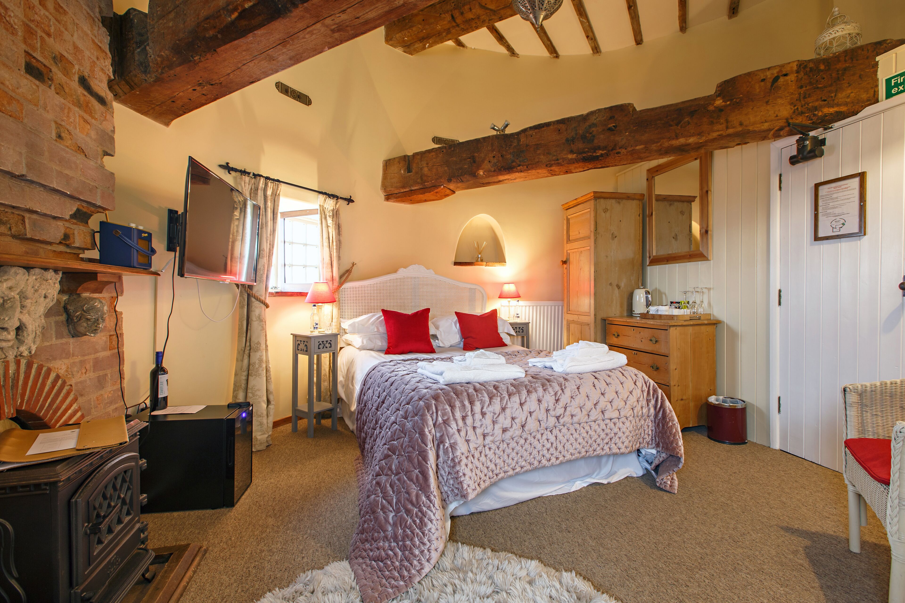 A cozy bedroom with a large bed, a wooden dresser, a television, and a fireplace.