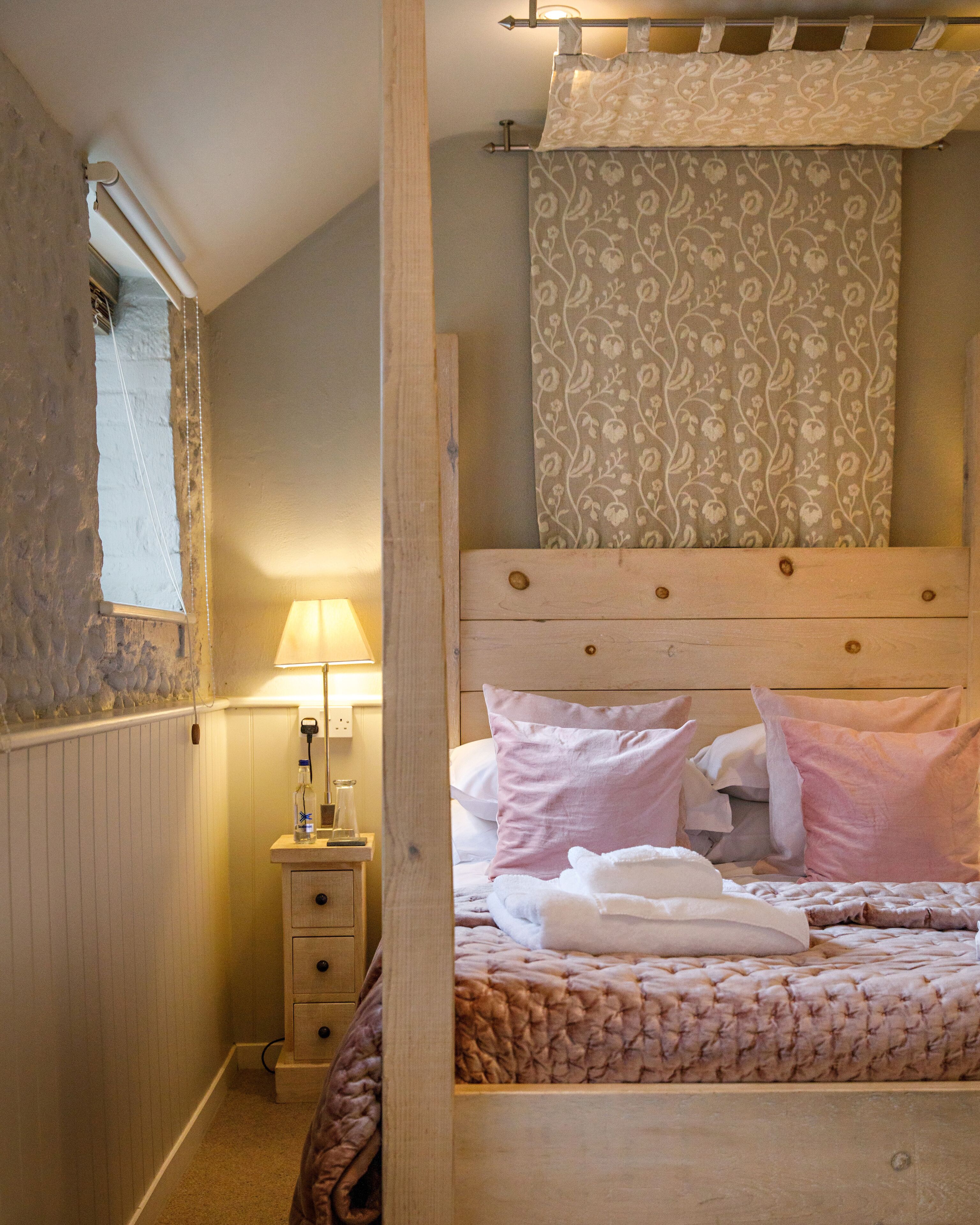 A bedroom with a wooden bed, a bedside table with a lamp, and a window with a curtain.