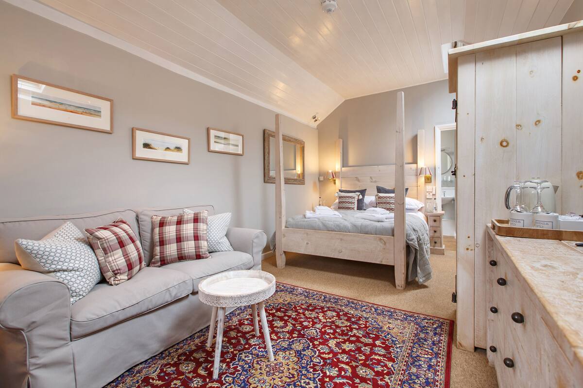 A bedroom with a bed, a sofa, a small table, and a large mirror.
