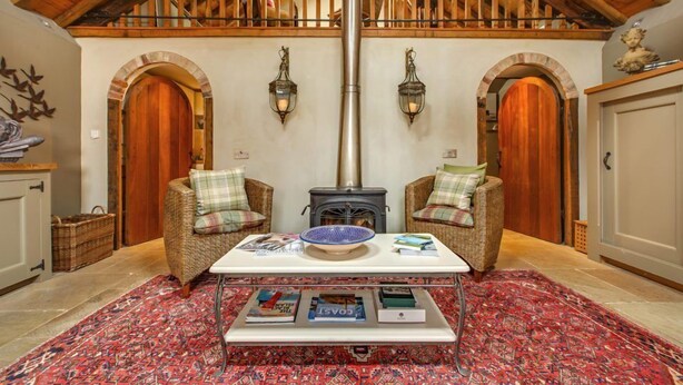 A cozy room with a high wooden ceiling, two wooden doors, a central table with books, a bowl, and a fireplace. - Cley Windmill (Holt)